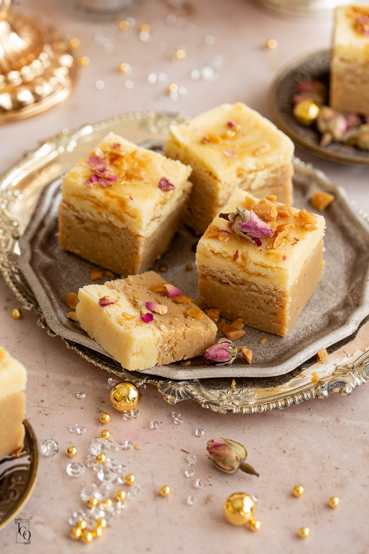 Three and a half pieces of 2 layer burfi decorated with rose petals, broken butter candies placed on a gold decorative tray. 
