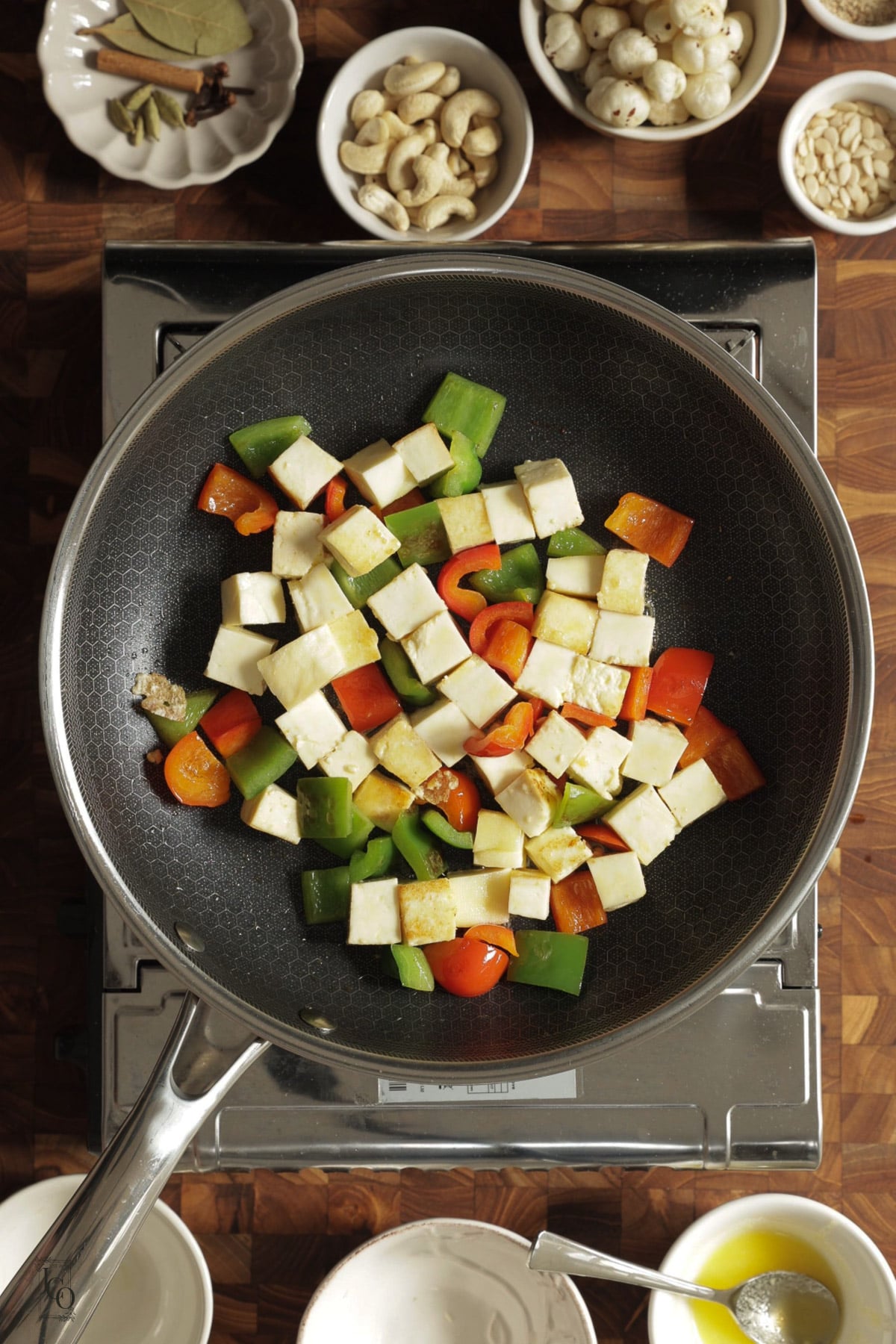 Green and red bell pepper and paneer cubes cooking in a pan.