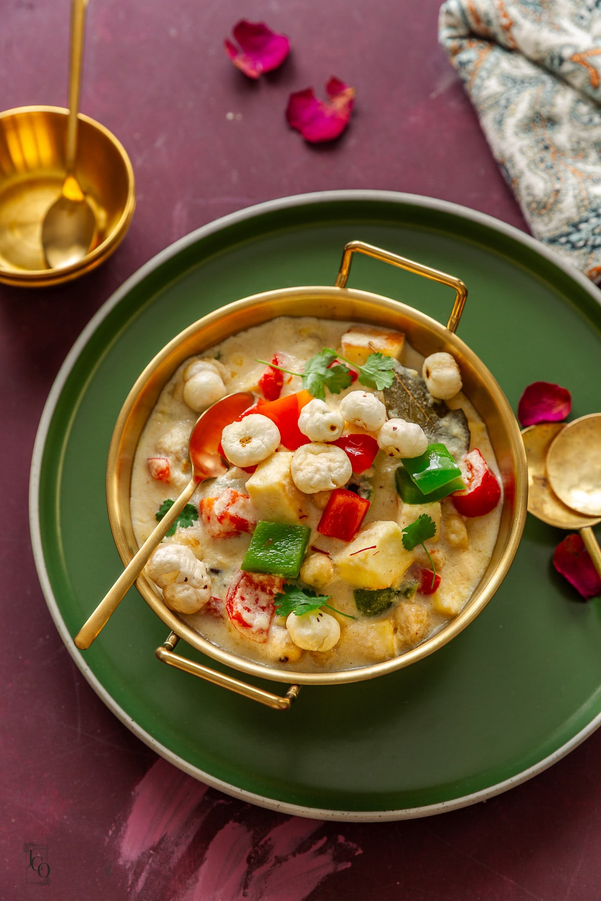 A bowl of white Indian paneer and makhana curry placed on a green plate.