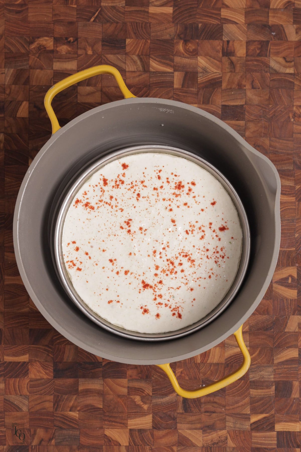 Semolina batter in a stainless steel tray, sprinkled with red chilli powder in a steamer pot.