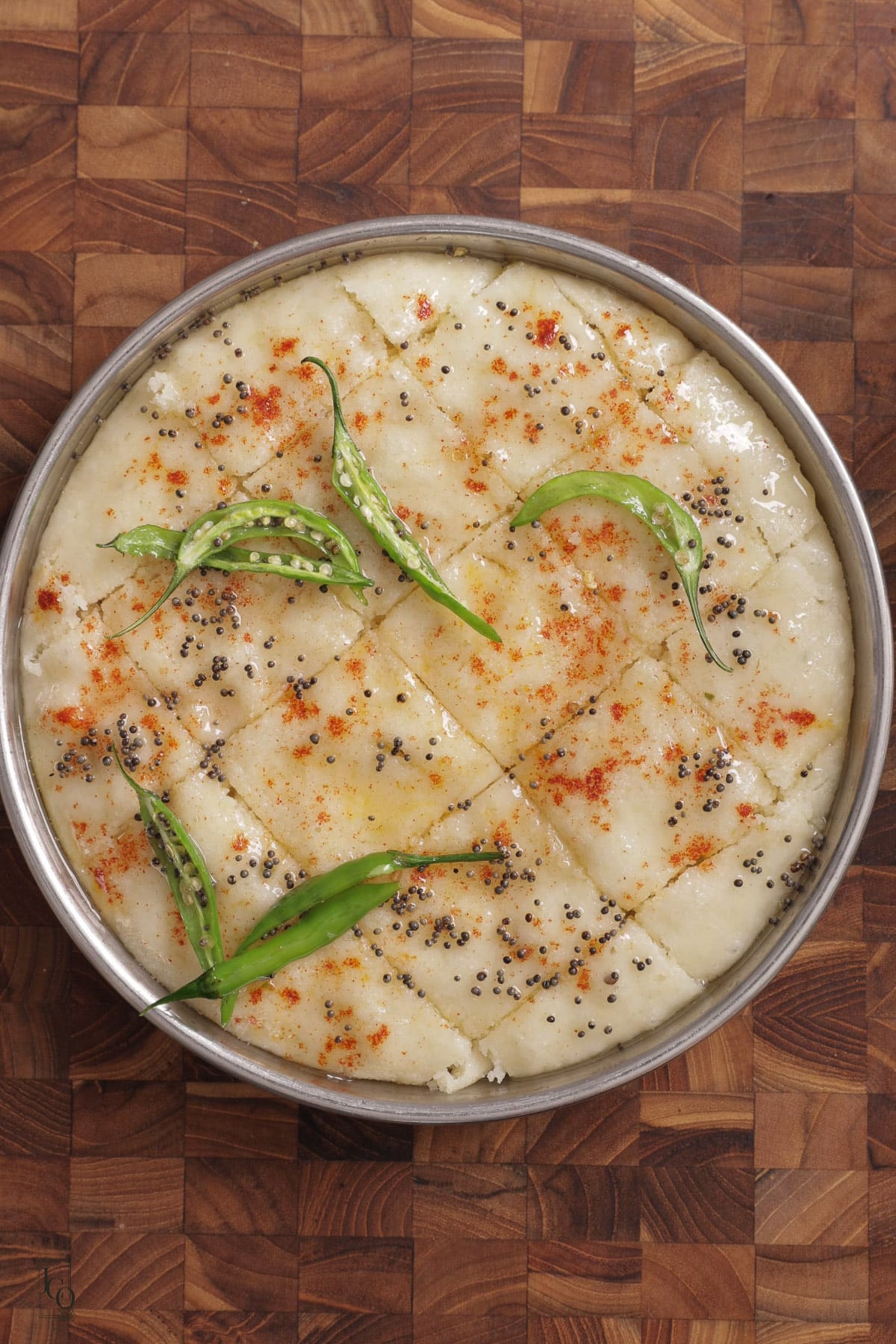 Mustard seeds and green chilli tempering poured over cut rava dhokla pieces.