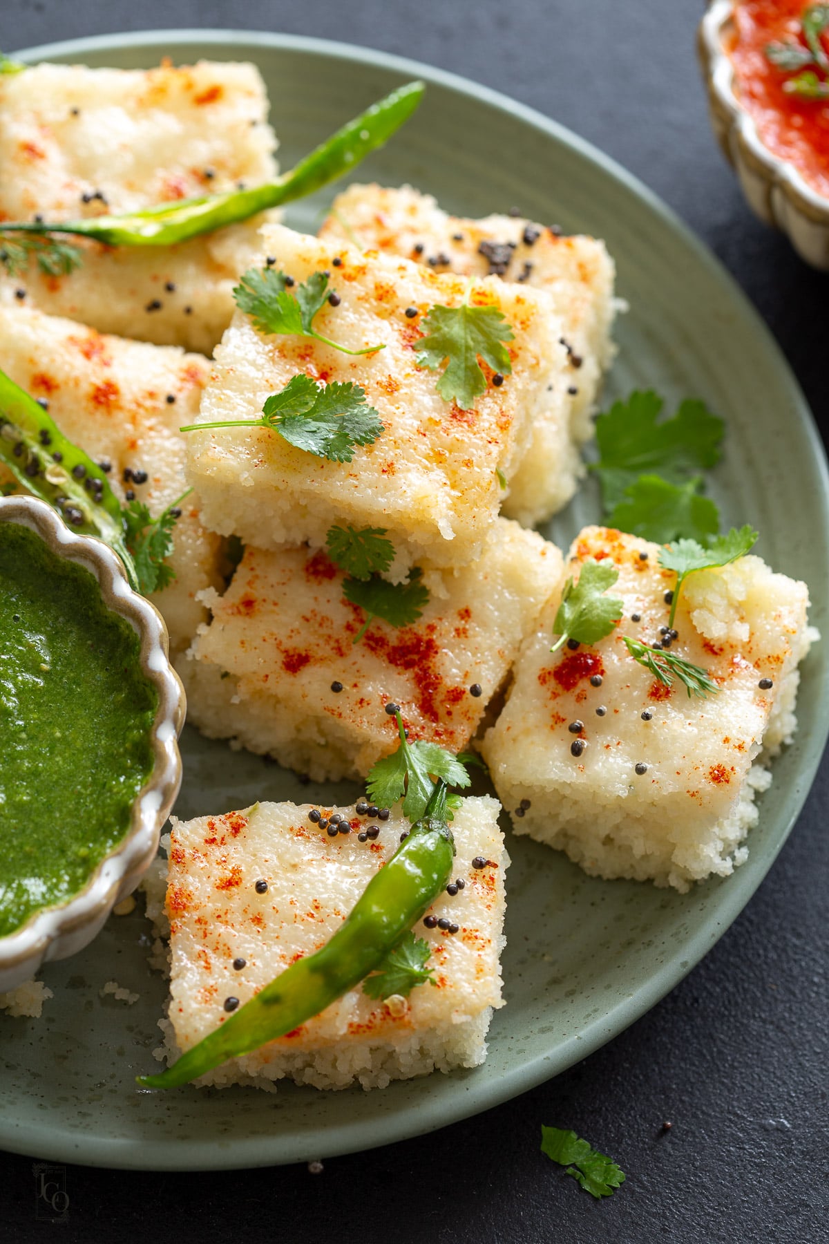 Stack of rava dhokla garnished with chopped coriander and slit green chillies.