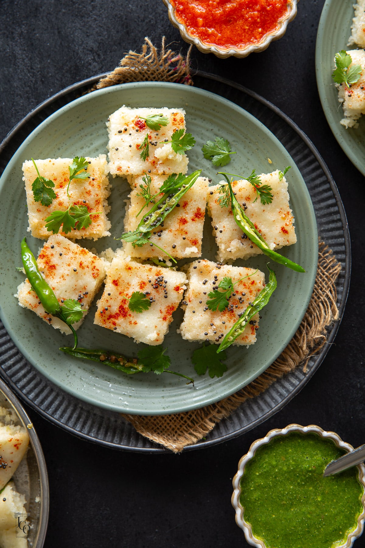 Six pieces of rava dhokla arranged on a green serving plate.