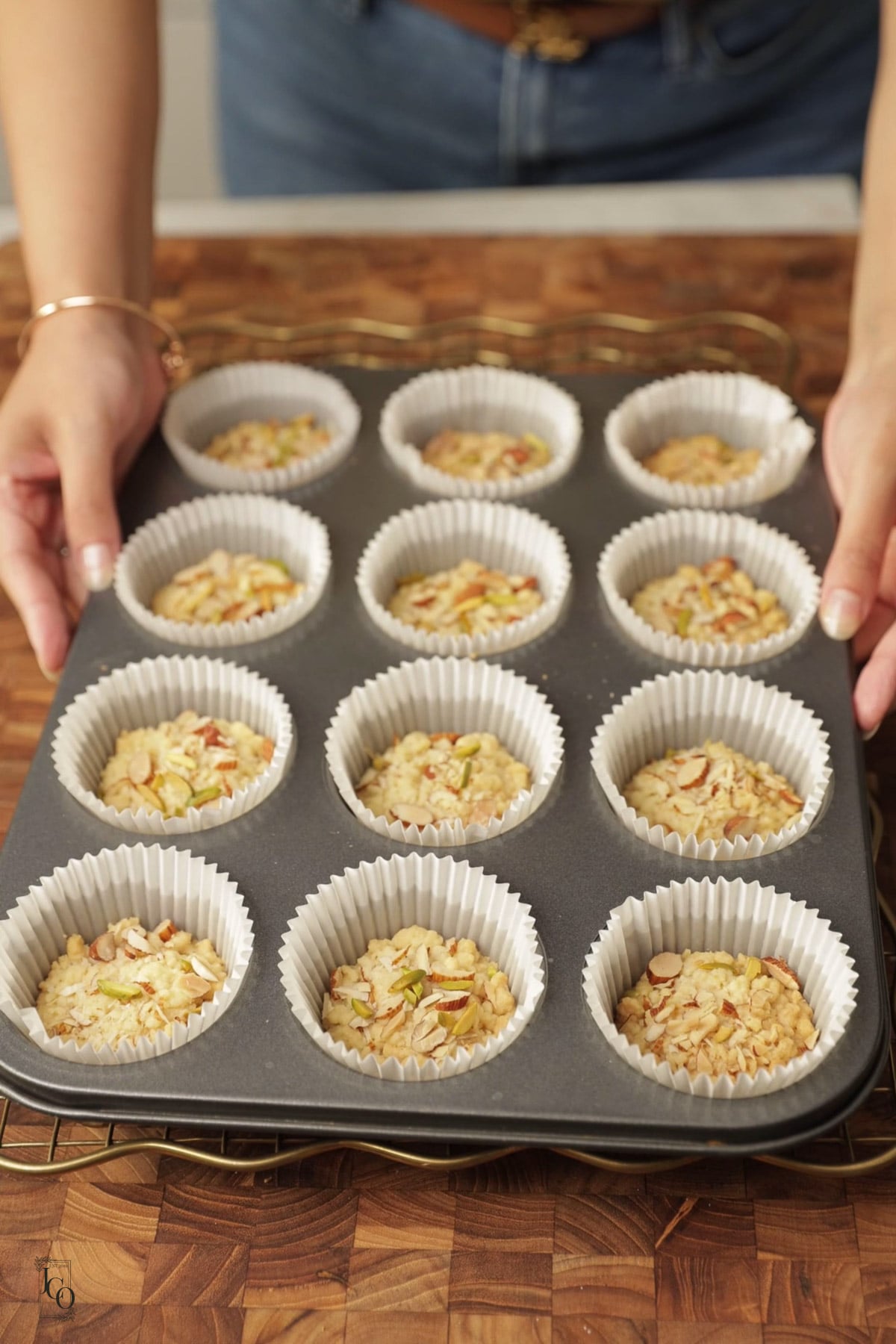 Female hands are holding a muffin tin that has twelve badam halwa shortbread cookies.