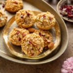 Badam halwa shortbread cookies decorated with rose petals and edible silver foil, arranged in decorative serving tray on the table.