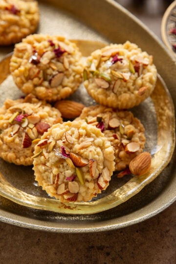 Badam halwa shortbread cookies decorated with rose petals and edible silver foil, arranged in decorative serving tray on the table.