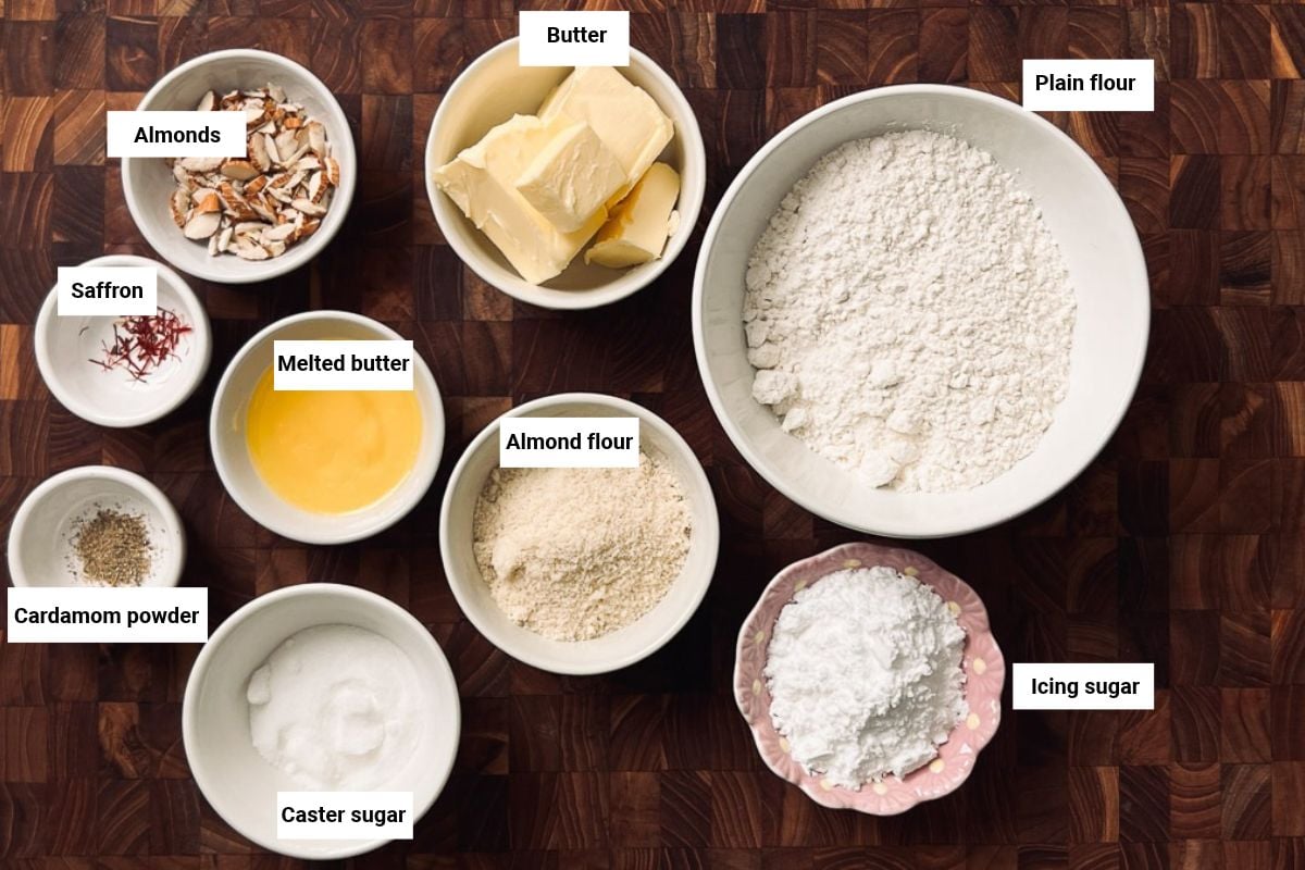 Plain flour, chopped almonds, almond flour, sugar, butter, saffron and cardamom in bowls.