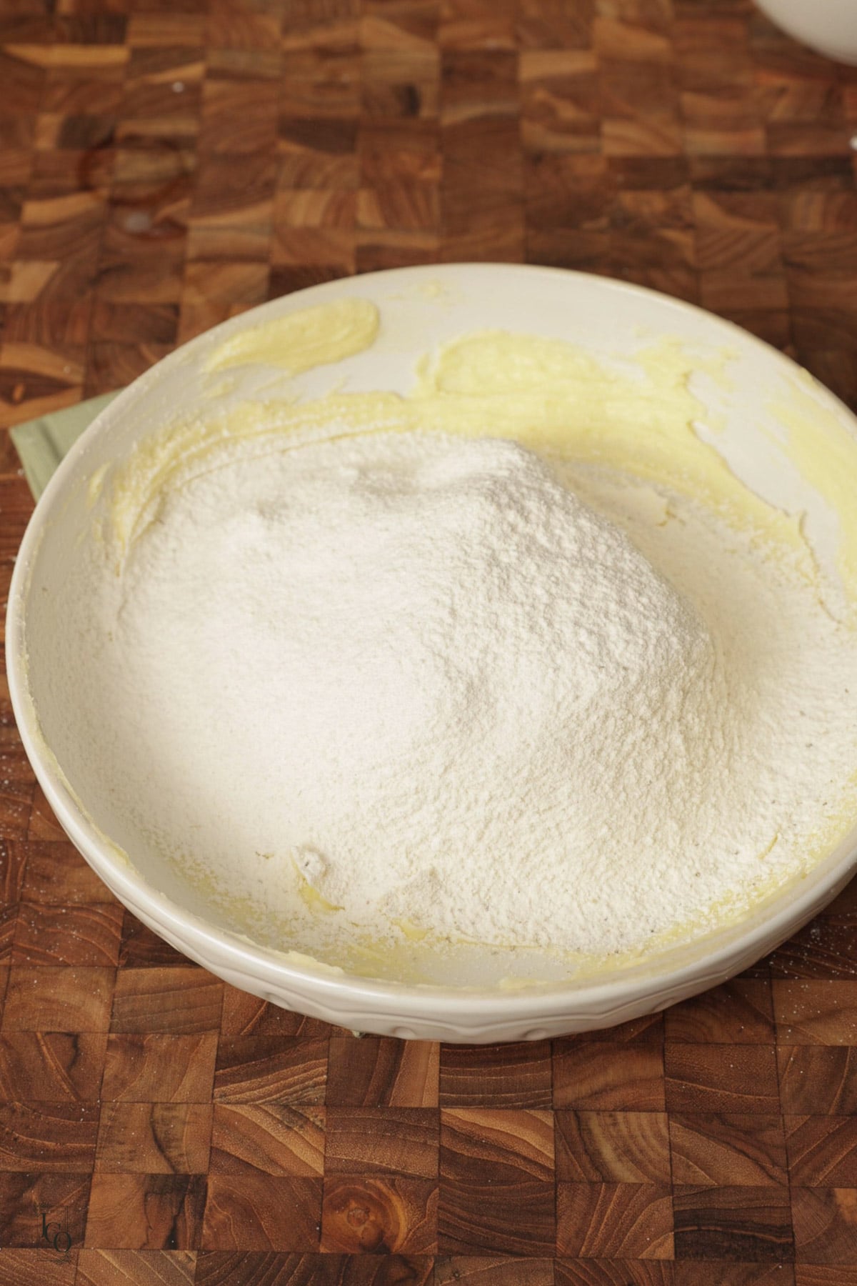 Sifted flour added to creamed butter and sugar in a bowl.