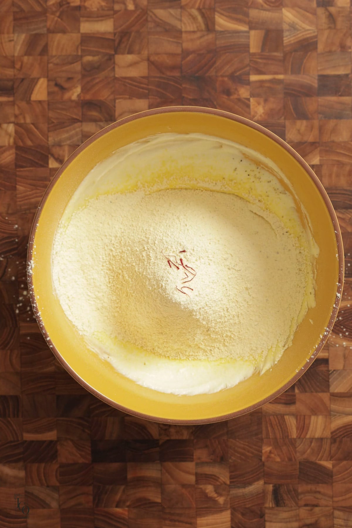 A yellow bowl containing creamy ghee mixture and a mound of besan topped with several saffron strands.