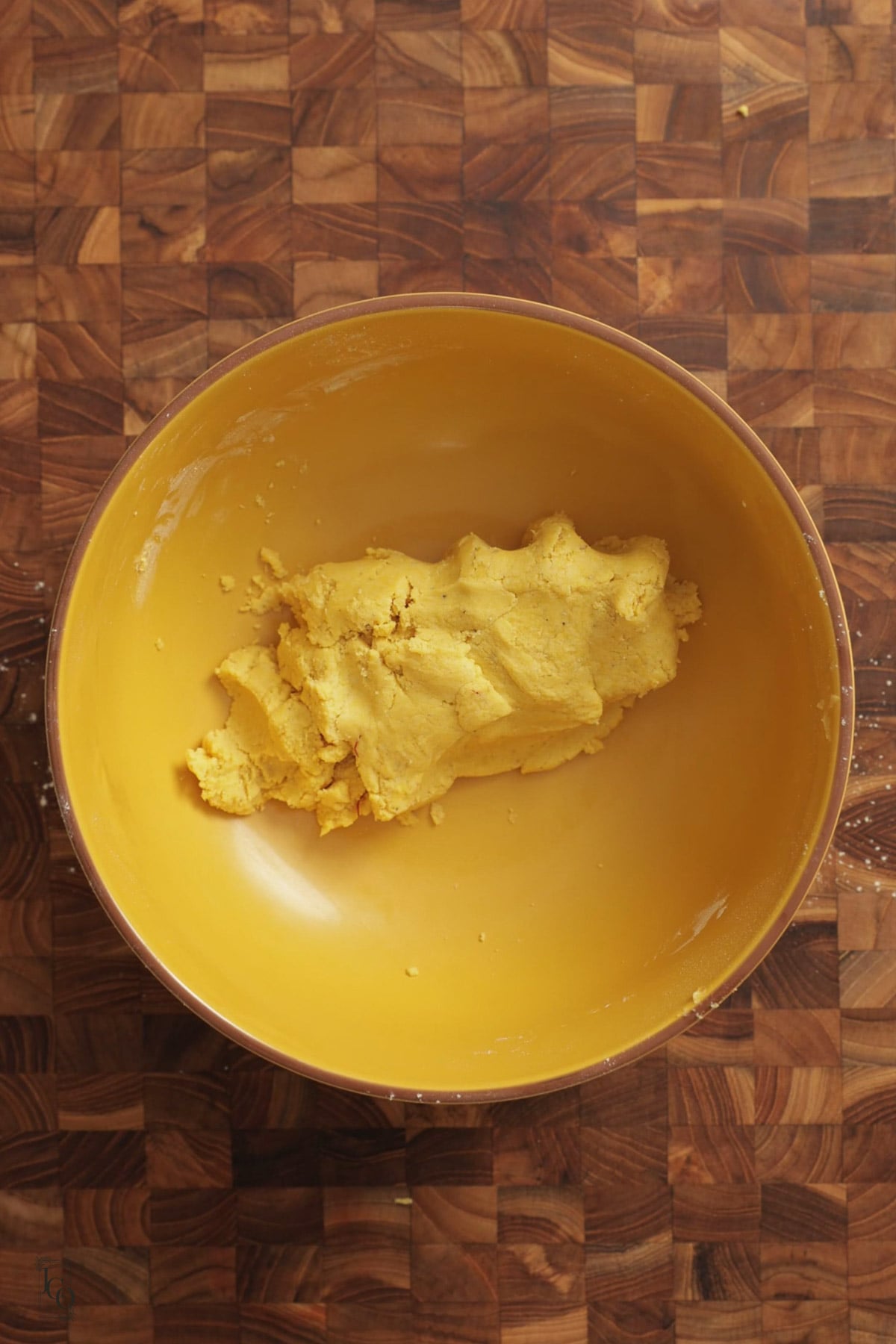 Soft besan nankhatai dough in a yellow bowl set on a wooden cutting board.