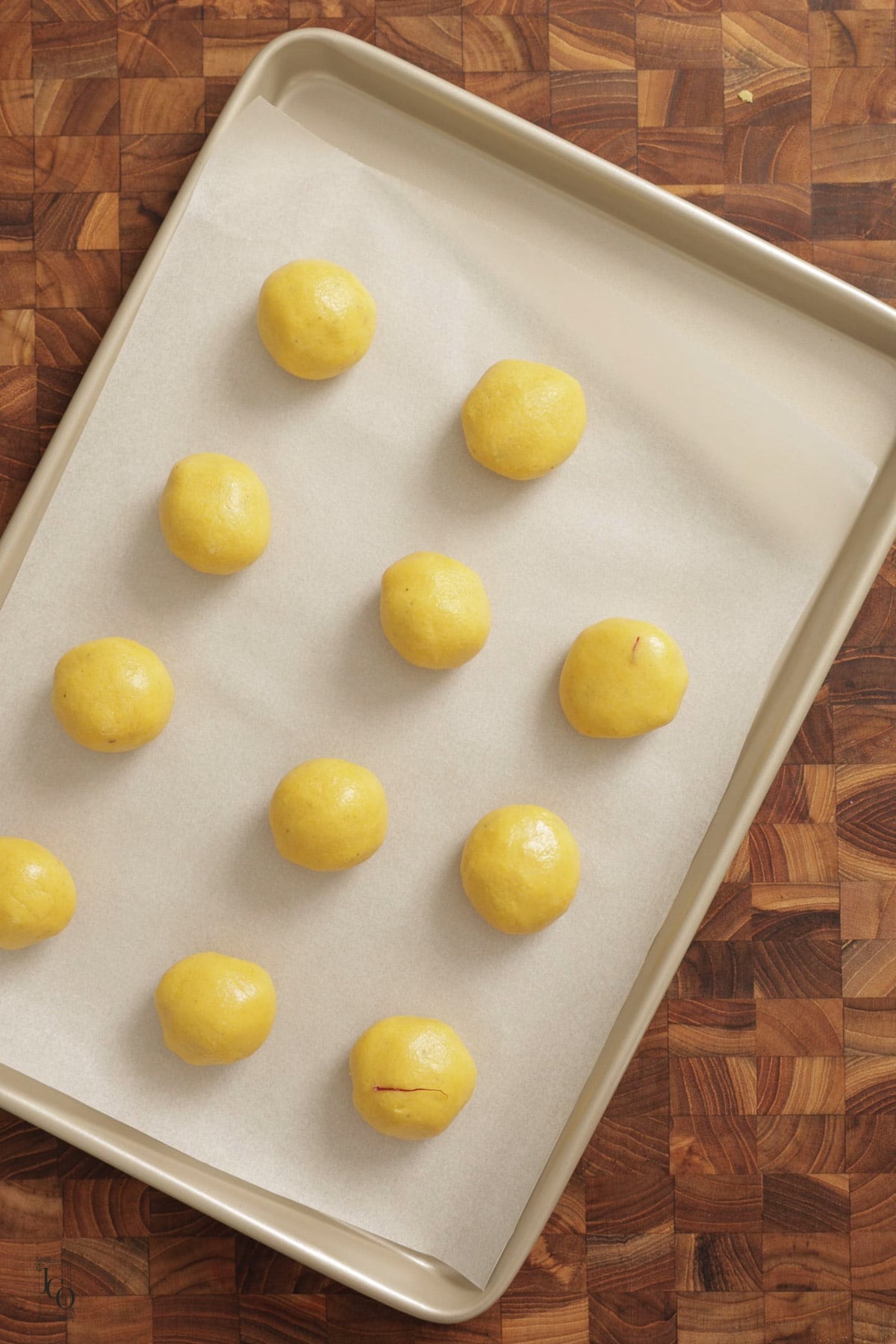 Eleven round, yellow besan nankhatai dough balls arranged on a parchment-lined baking sheet.