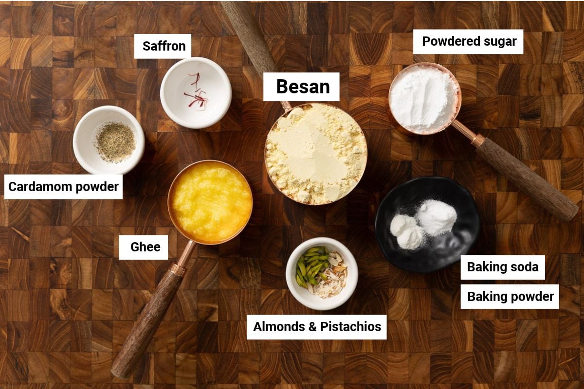 Gram flour, ghee, sugar, spices and baking soda in bowls. 