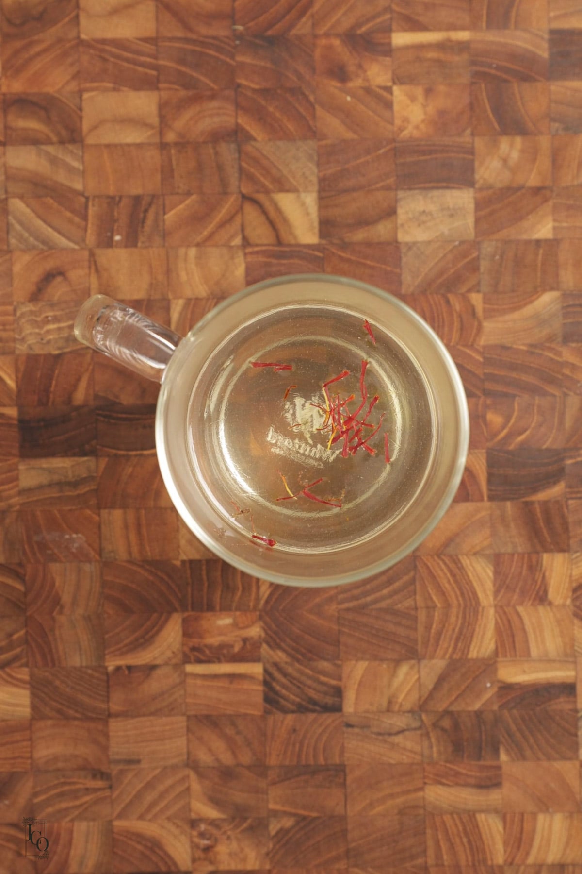 Saffron strands added to the warm cardamom syrup in a clear glass.