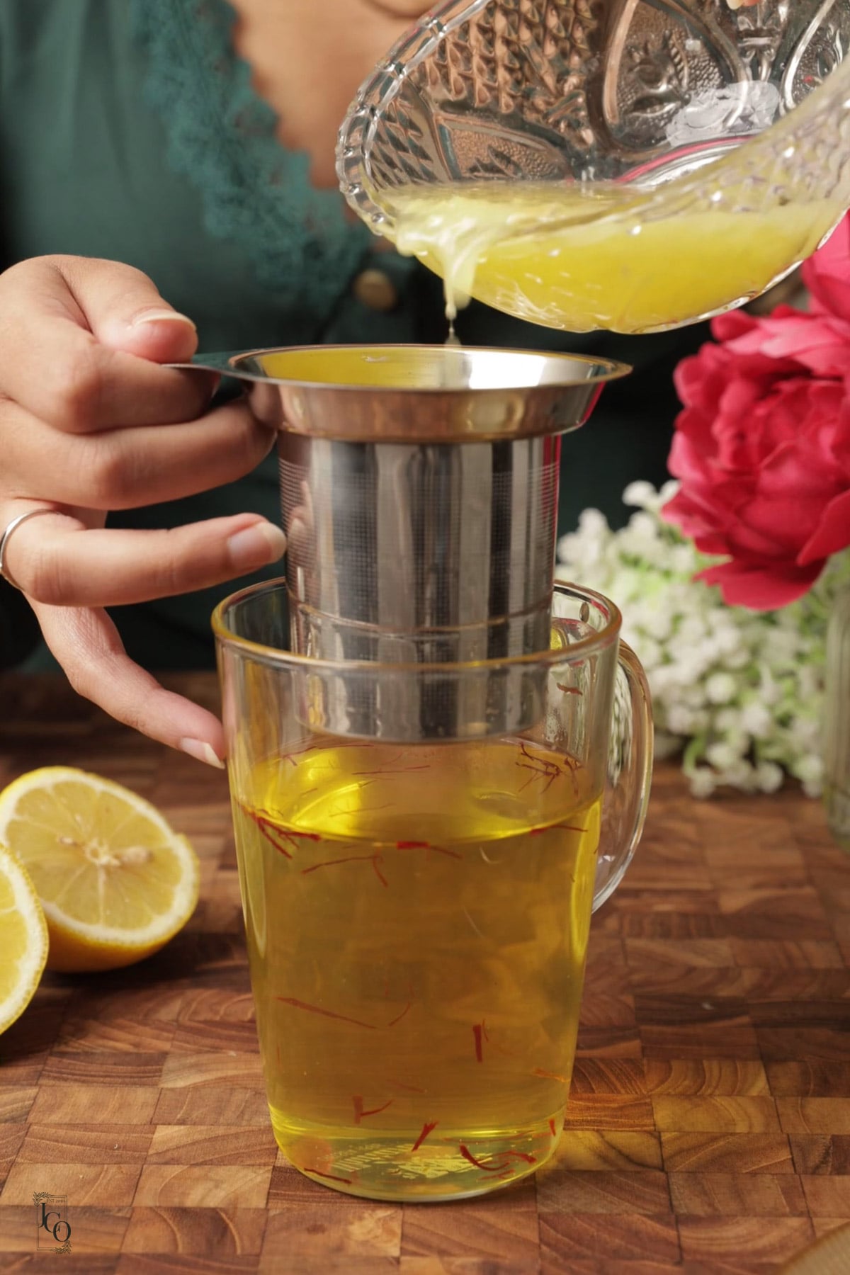 A female hand is pouring lemon juice through tea strainer into saffron syrup.