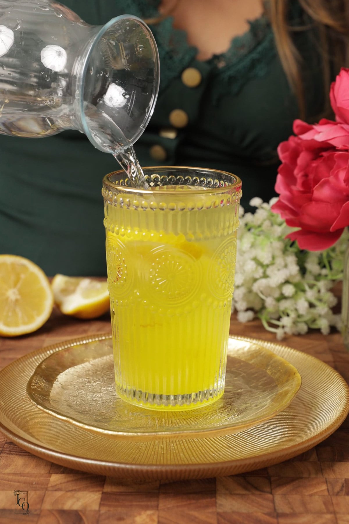 A female hand is pouring water into a glass over the saffron syrup.