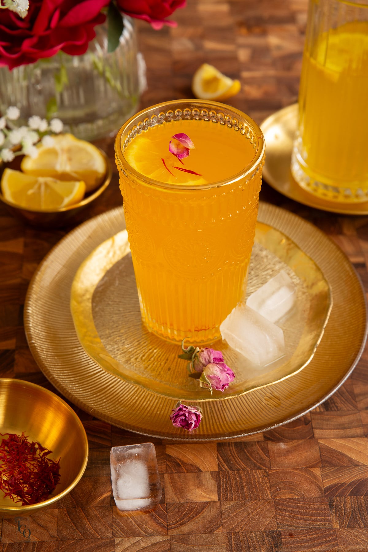 Three ice cubes placed around a glass of saffron lemonade on a gold tray.